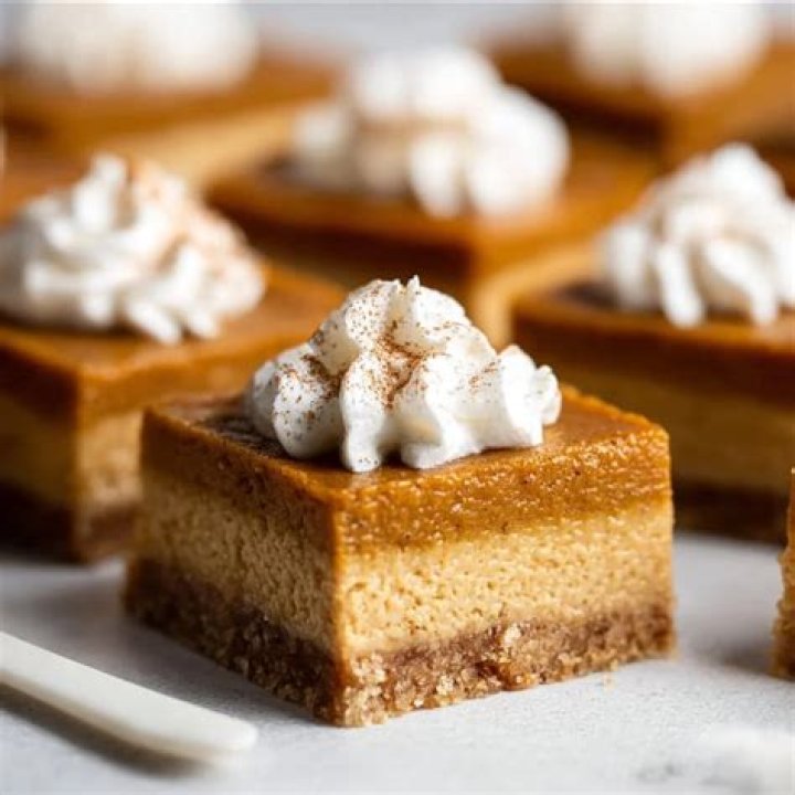 Pumpkin pie bars topped with whipped cream on a white plate.